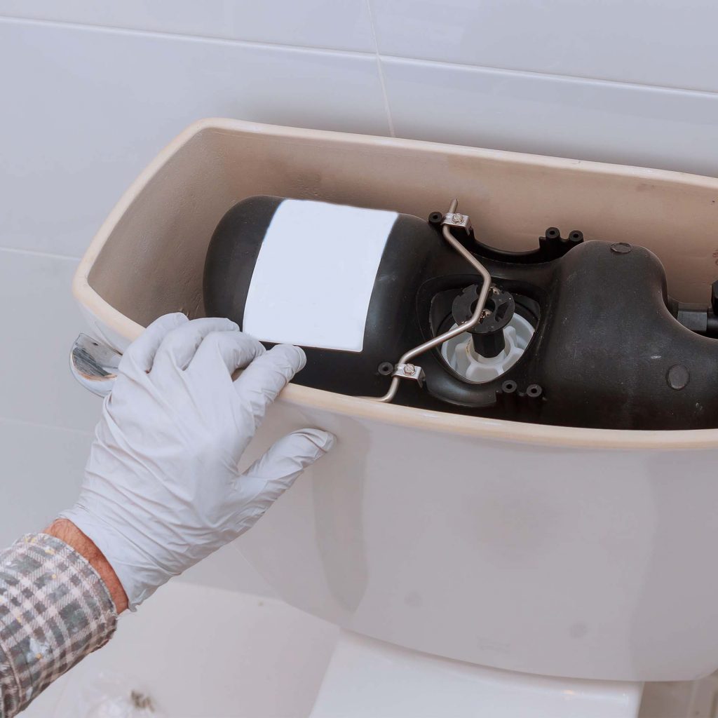 Hand resting on top of upper toilet tank with the lid off.